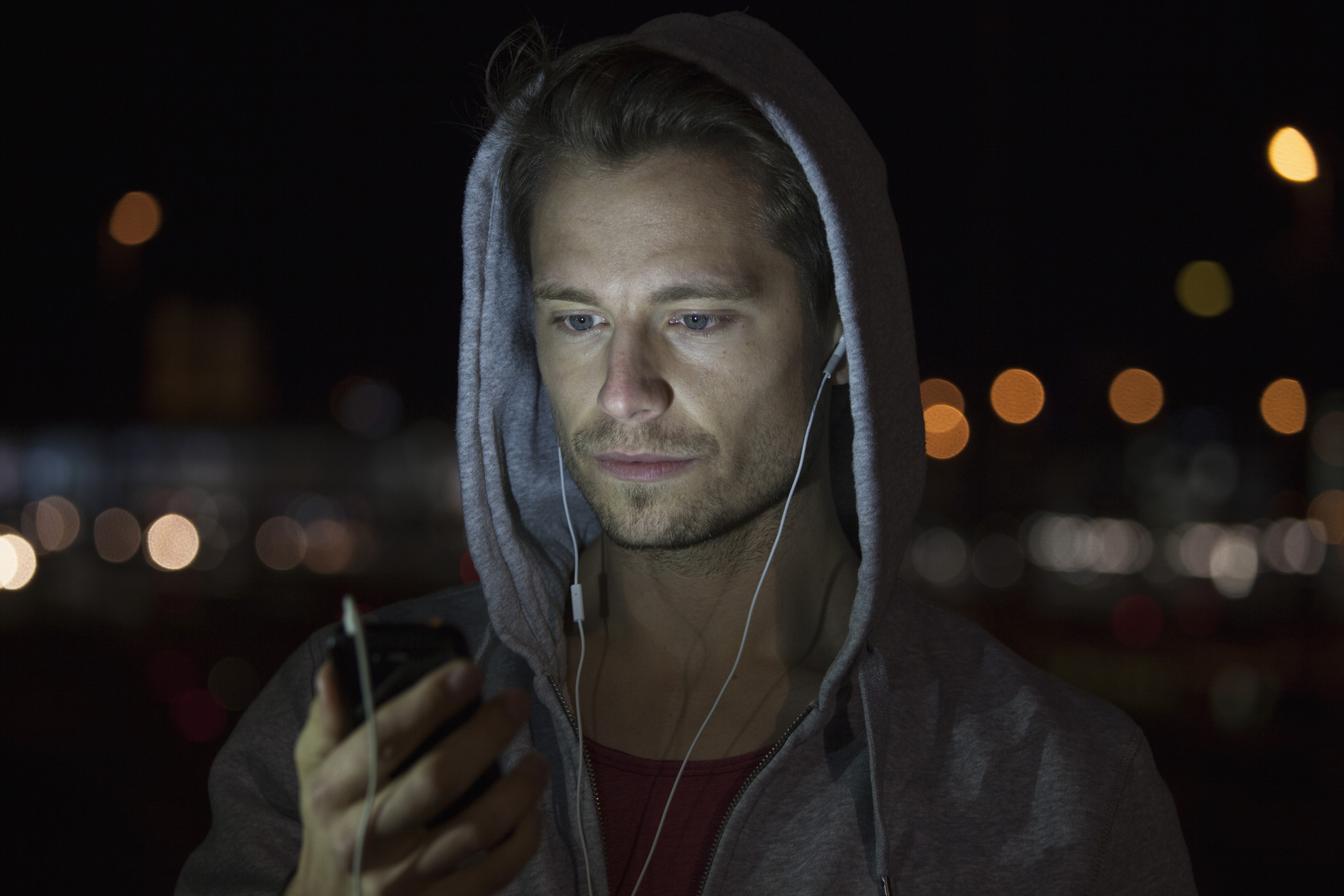 Portrait of young man wearing hooded jacket listening music at night